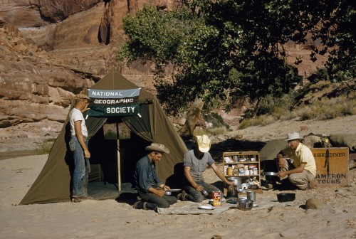 Men eat outside chow tent at remote campsite.