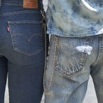 A close up of two people's back pockets. The person on the left has their hands in their back pockets and they wear dark wash Levi's® jeans. The person on the right has their right hand in their right back pocket and they wear light acid wash Levi's® jeans with a silver chain hanging on their left side.