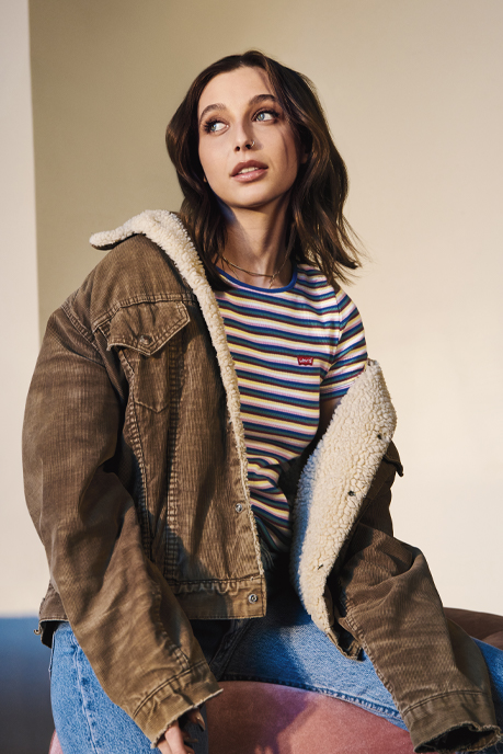 Emma Champerlain poses in a striped Levi's® T-shirt and a brown sherpa-lined Levi's® jacket for the Levi's® "Buy Better, Wear Longer" campaign.