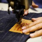 A pair of hands works at a sewing machine to sew a Levi's® leather patch onto the back of a pair of Levi's® denim jeans.