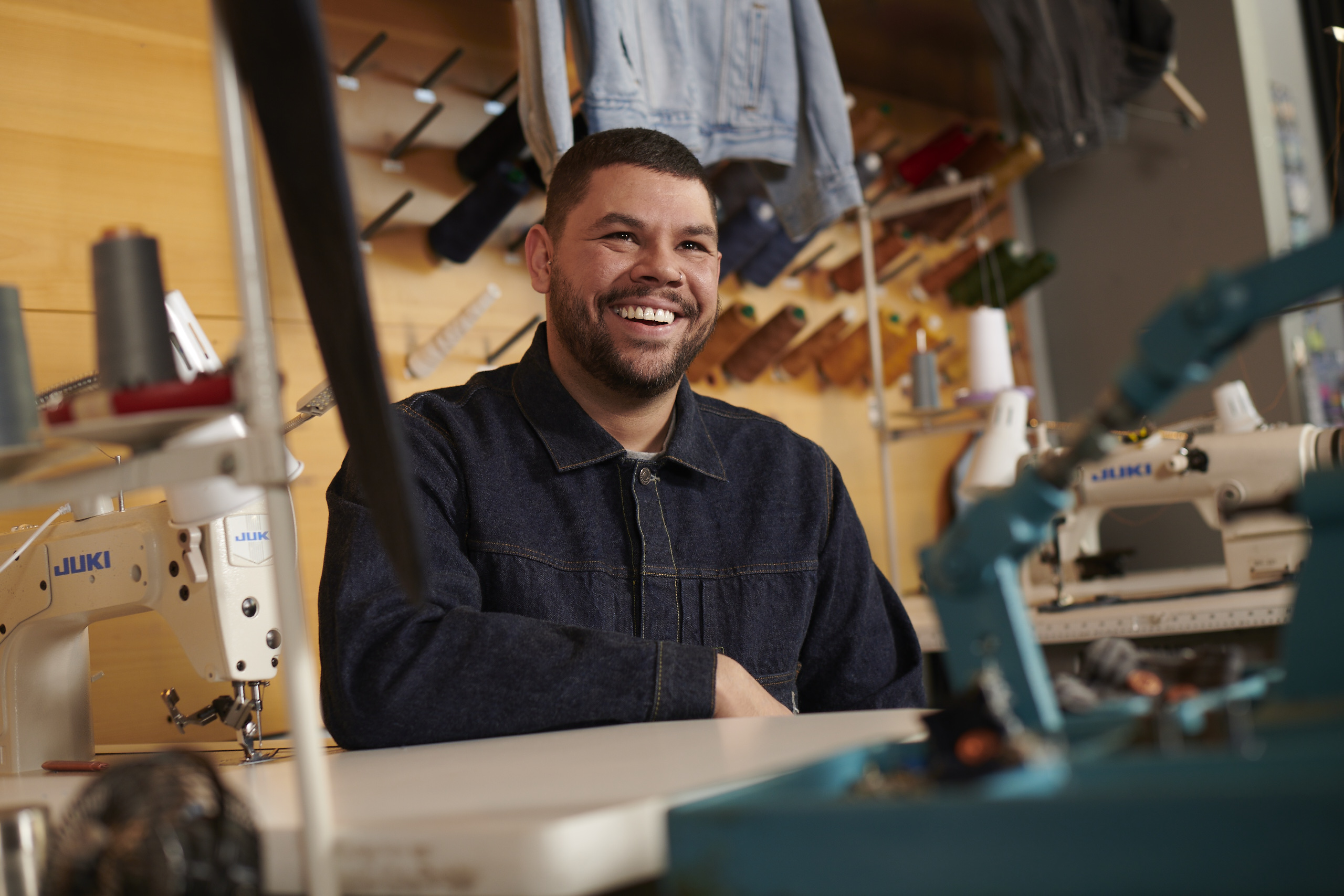 A Levi's® Tailor sits at a Tailorshop workstation and smiles.