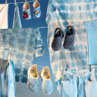 Three pairs of Levi's® Crocs hang on a stacked clothesline next to hanging tie-dye printed fabric.