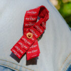 A close up of a red ribbon made of Levi's® red tabs on a light wash denim jacket.The red ribbon is the universal symbol of awareness and support for people living with HIV.