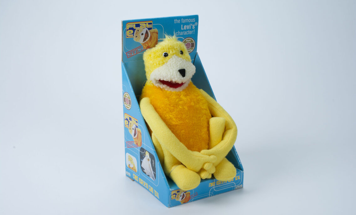 "Flat Eric," a yellow plush puppet, sits packaged in a box.