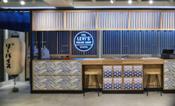 The Levi's® Tailor Shop in the Levi's® Kyoto store, featuring a circular neon sign reading "The Levi's® Tailor Shop Kyoto" in light blue lettering, wood paneling, a Japanese lantern and a table with Japanese-inspired designs. 