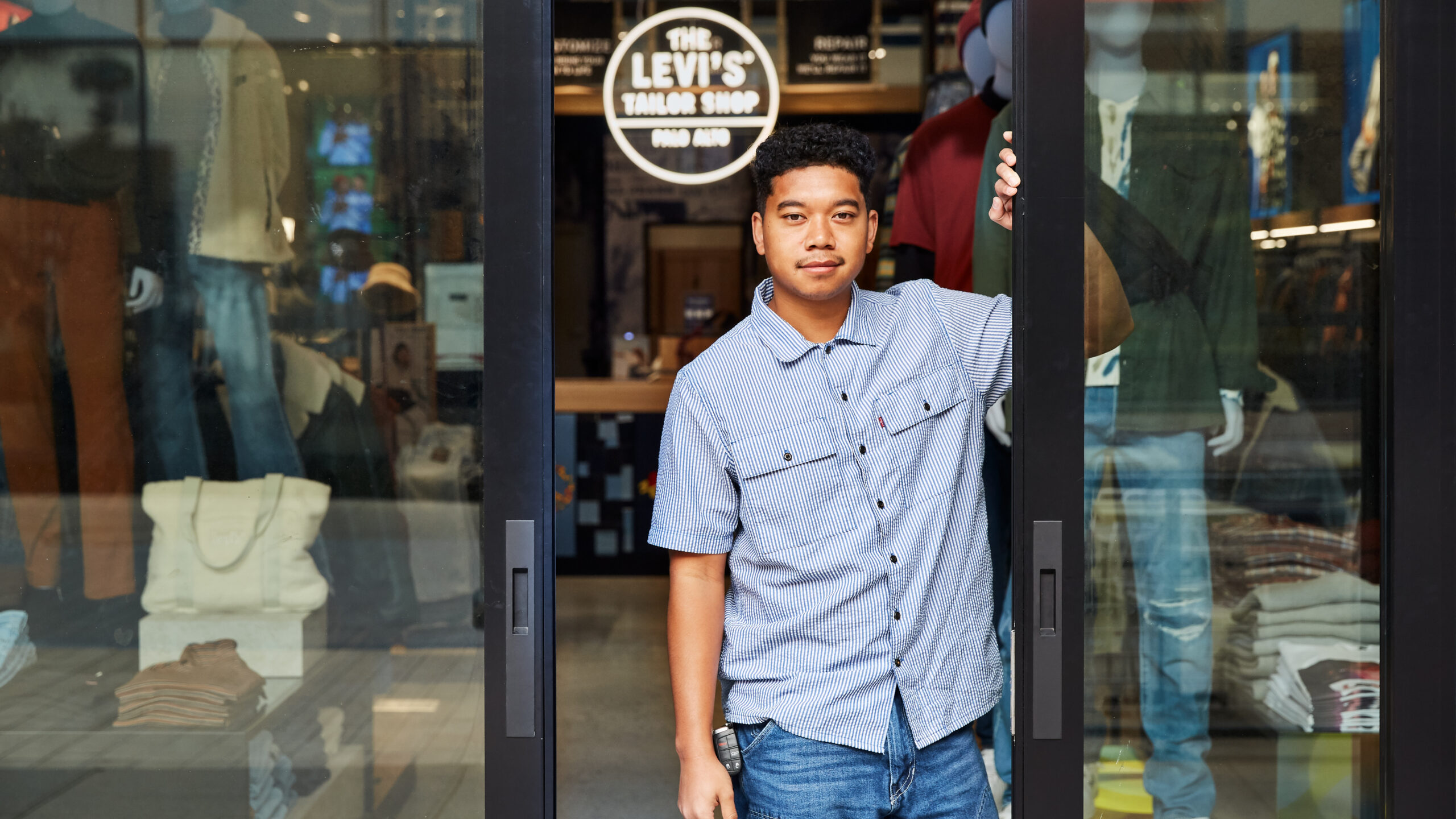 A Levi's® retail worker smiles at the front door of a Levi's® store.
