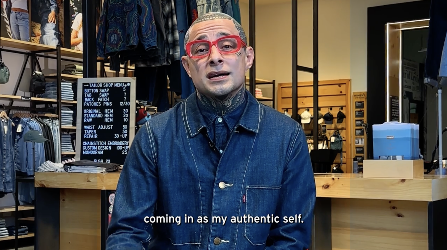 Levi's® Century City Store Manager Angel Mendoza sits in the Levi's® Tailor Shop. He is wearing red rimmed glasses and a Levi's® blue denim top. A subtitle appears on the bottom of the image in white text 