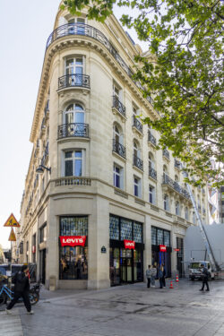 The exterior of Levi's® Champs-Élysées in Paris. A cream colored Parisian-style building stands at five stories tall with a Levi's® storefront on the ground floor. The red Levi's® logo repeats across windows on the ground floor. 