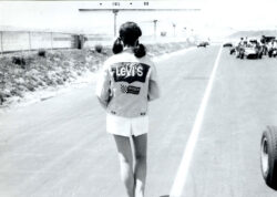 A black and white photo of a person turned away from the camera running on a racetrack and wearing a Levi's® logo jacket and white shorts.