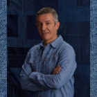 LS&Co. Chief Commercial Officer Gianluca Flore smiles and poses with his arms crossed in front of a blue background. The photo is imposed on top of a blue denim background.