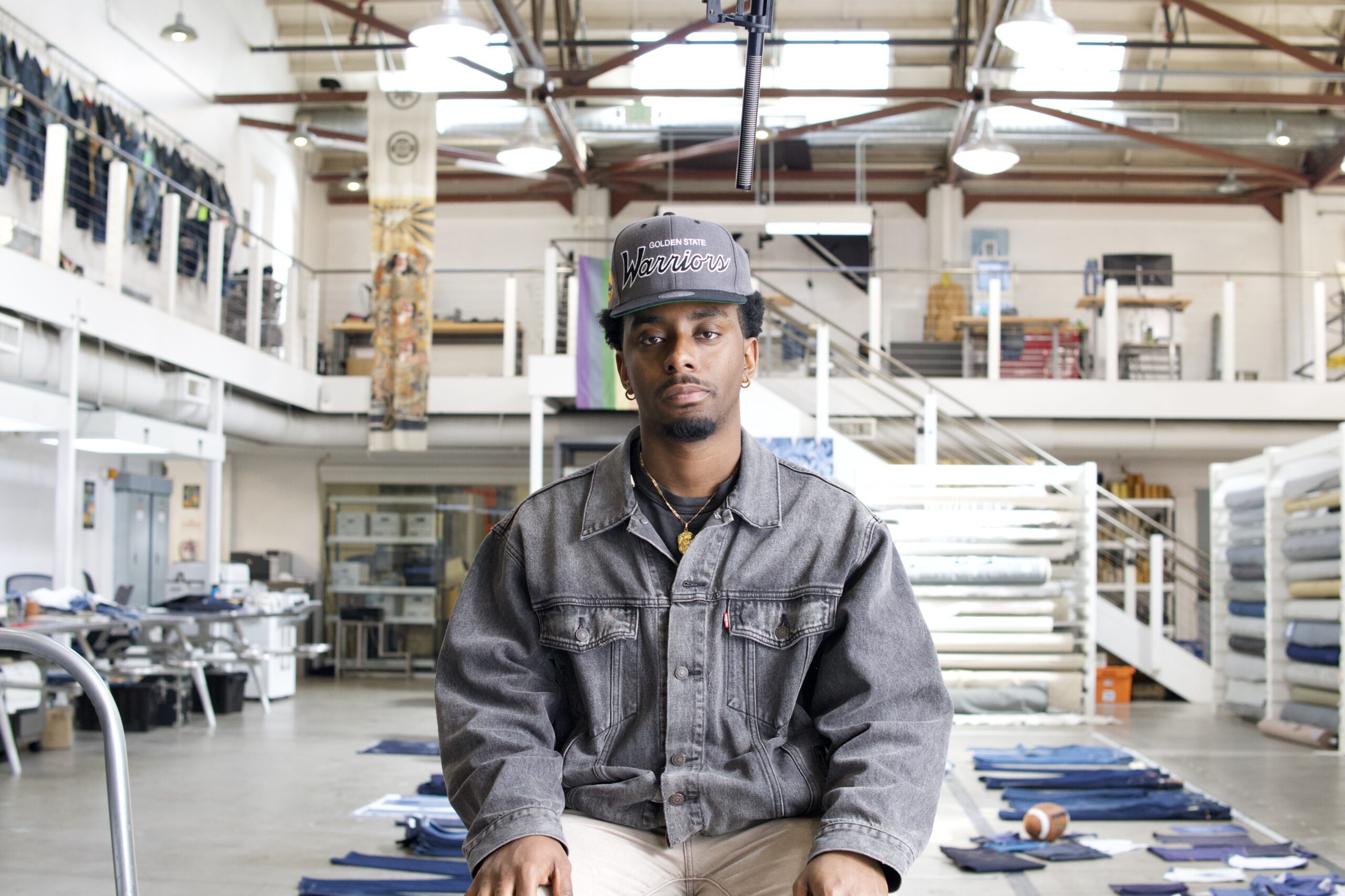 An LS&Co. employee faces the camera and sits on inside the Eureka Innovation Lab. He wears a grey Golden State Warriors hat and a faded black Levi's® Trucker jacket.