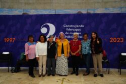 Members of Red de Mujeres Sindicalistas (RMS) pose in front of a blue and purple screen.