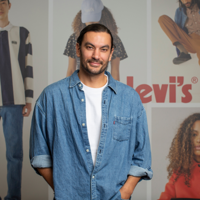 An LS&Co. employee poses in front of a Levi's® product background wearing a blue denim shirt over a white t-shirt