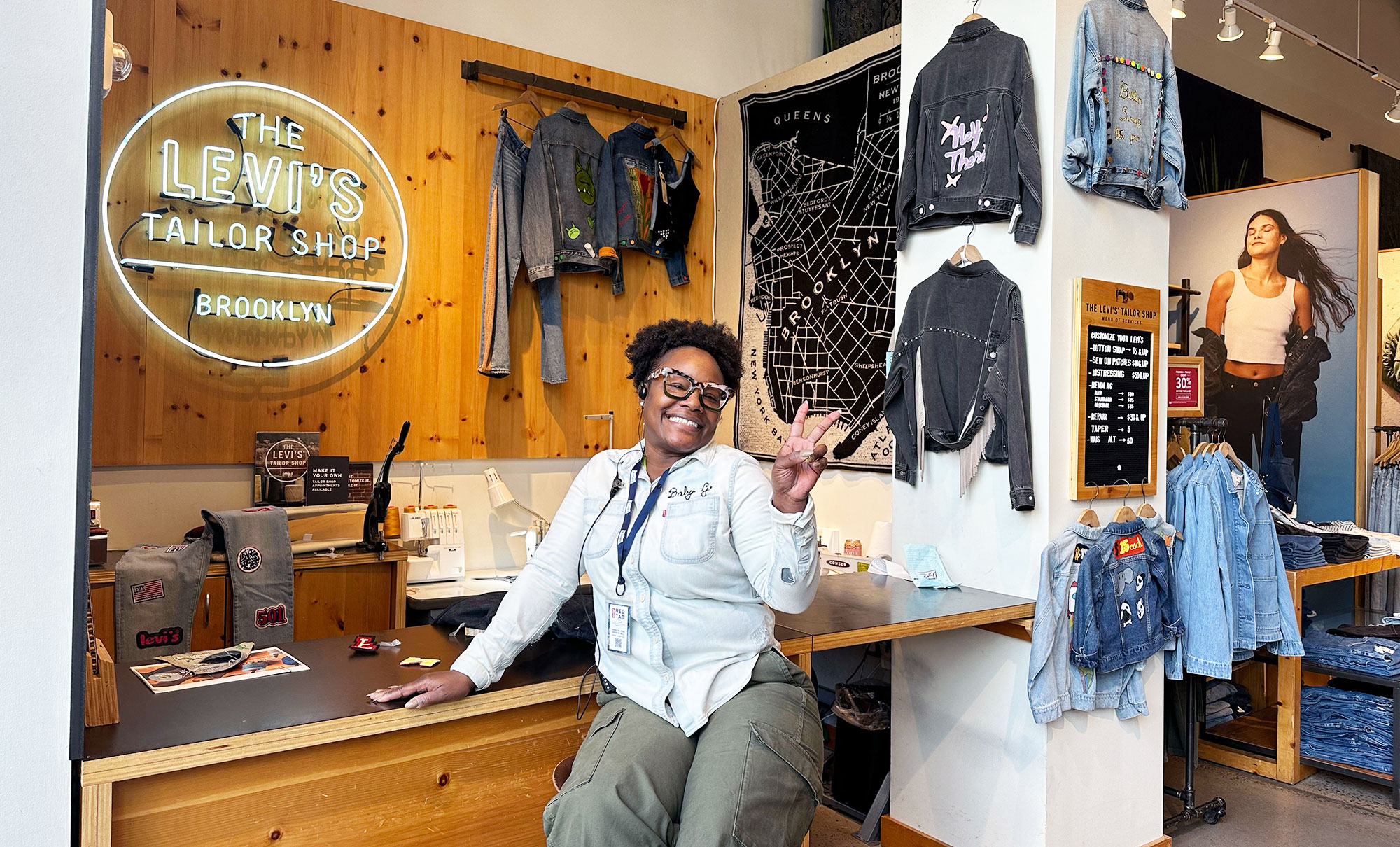 Levi's® Store Manager Gladys Jennings smiles and shows a peace sign while sitting at the Levi's® Williamsburg Tailor Shop.