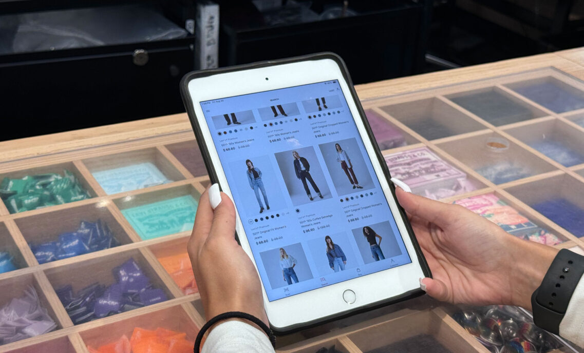 A person's hands hold a tablet featuring a grid of Levi's® products on models with product names and information.