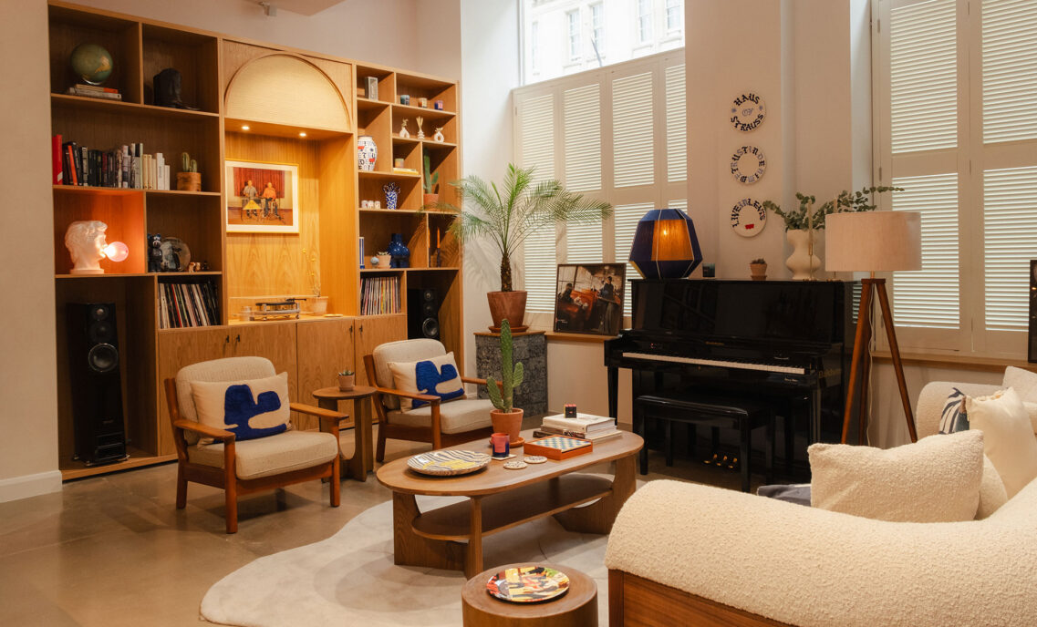 An interior space inside Haus of Strauss London, featuring built in shelves, arm chairs, coffee table, piano and sofa.