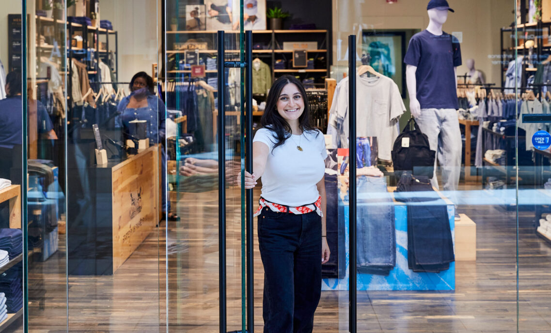 A Levi's® store employee opens the front door of a Levi's® store and smiles at the camera