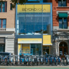 The exterior facade of Club Beyond, an experiential and retail pop-up from Beyond Yoga® in New York City. A rack of city bikes line a station in the foreground, in front of a two story building with open windows and a large Beyond Yoga sign.