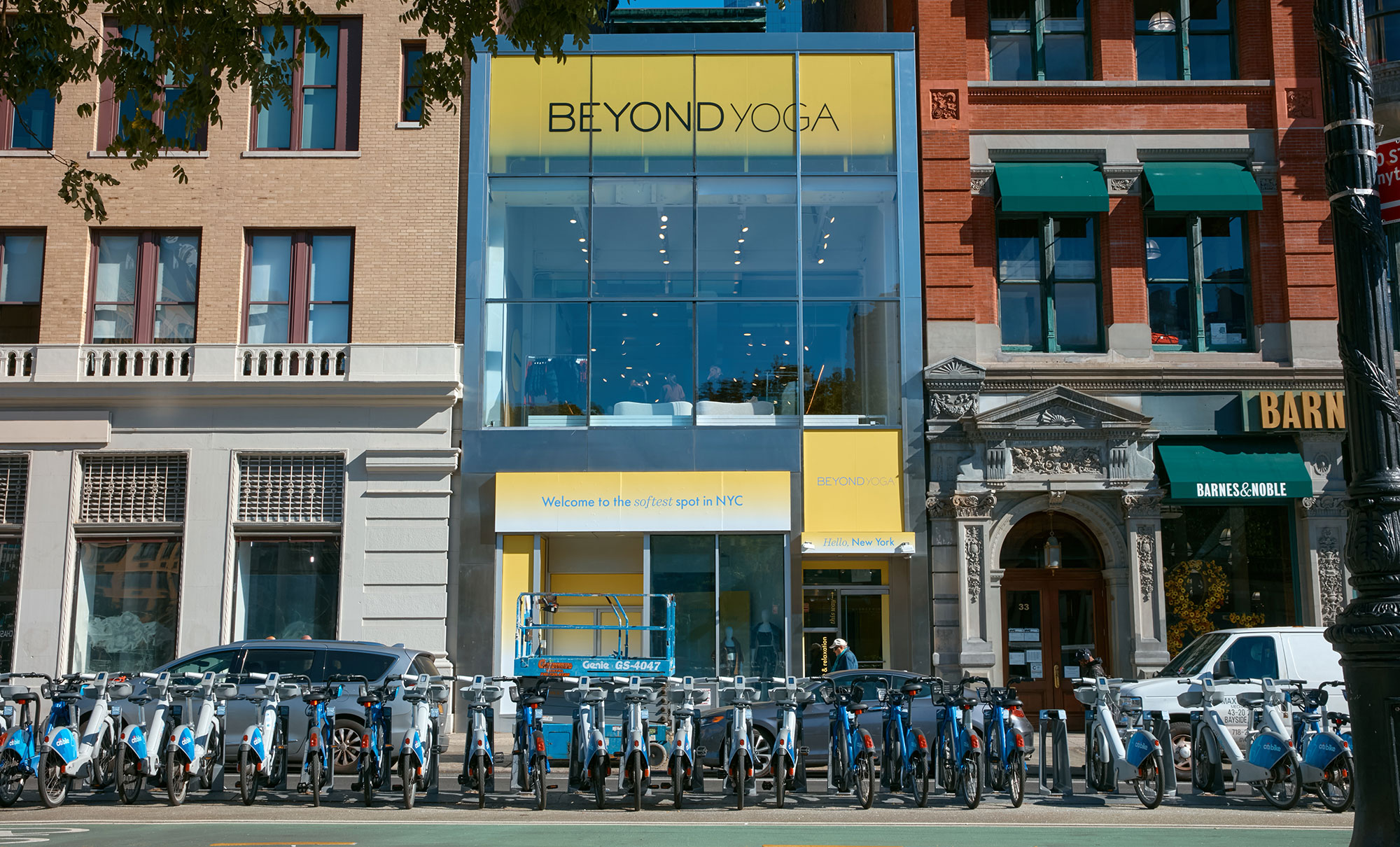 The exterior facade of Club Beyond, an experiential and retail pop-up from Beyond Yoga® in New York City. A rack of city bikes line a station in the foreground, in front of a two story building with open windows and a large Beyond Yoga sign.