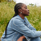 A person wearing a Levi's® denim jacket sits in a grassy field and looks off to the right