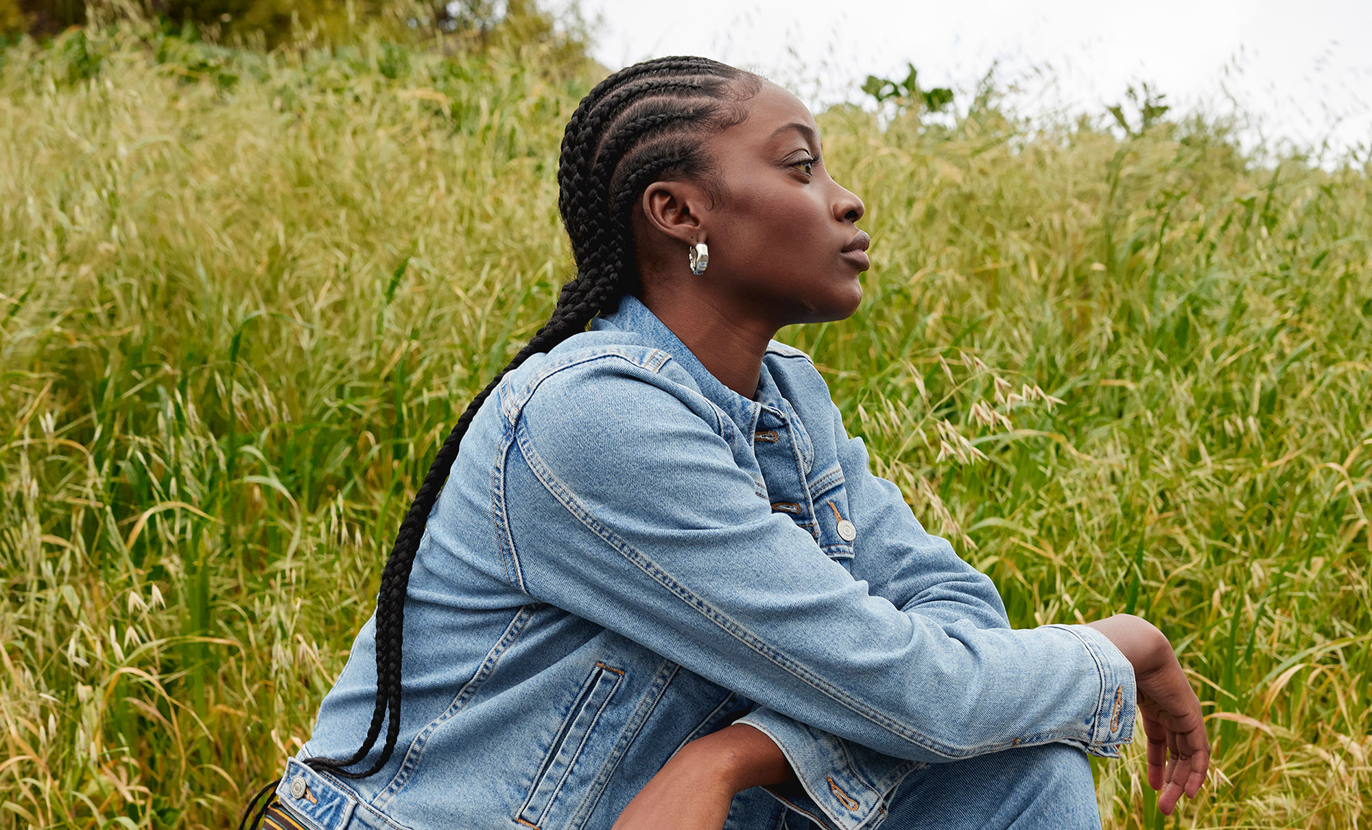 A person wearing a Levi's® denim jacket sits in a grassy field and looks off to the right