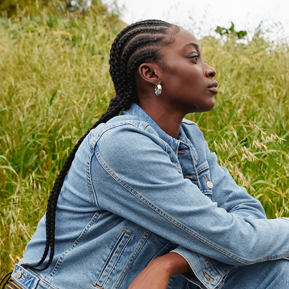 A person wearing a Levi's® denim jacket sits in a grassy field and looks off to the right