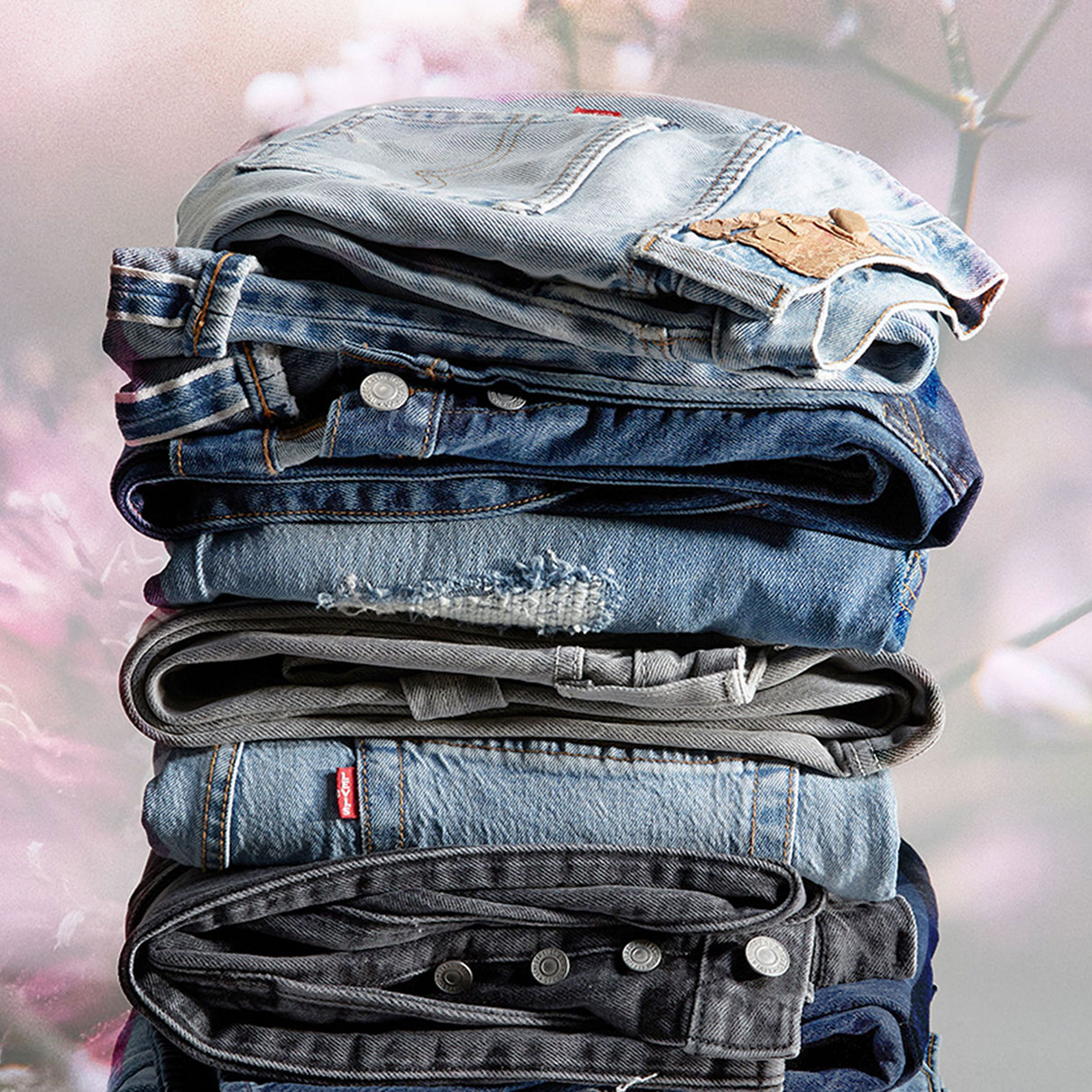 A stack of folded Levi's® denim jean sin various washes with a washed out floral background