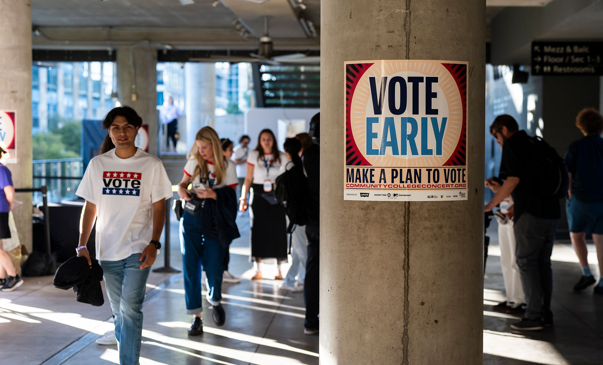 A person wearing a "Vote" T-shirt walks next to a column featuring a poster reading "Vote Early"