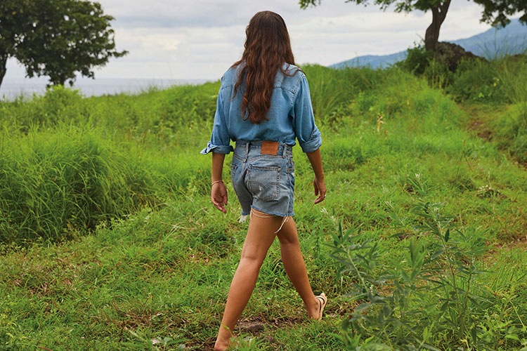 A person walks away from the camera in a grassy field wearing Levi's® denim shorts and a denim top.