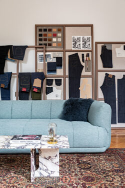 An interior space inside the Levi's® Haus of Strauss Paris. A sky blue plush sofa with a denim blue feathered pillow sits in front of a wall displaying various Levi's® jeans and Levi's® samples.