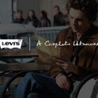 Timothée Chalamet as Bob Dylan in the upcoming biopic "A Complete Unknown," sitting on a bench reading a piece of paper. The image is overlaid with a white Levi's logo and the text "A Complete Unknown"