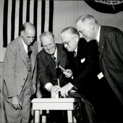 A black and white image of LS&Co.'s first vice president, Dan Koshland, and three other LS&Co. leaders gathered around a podium