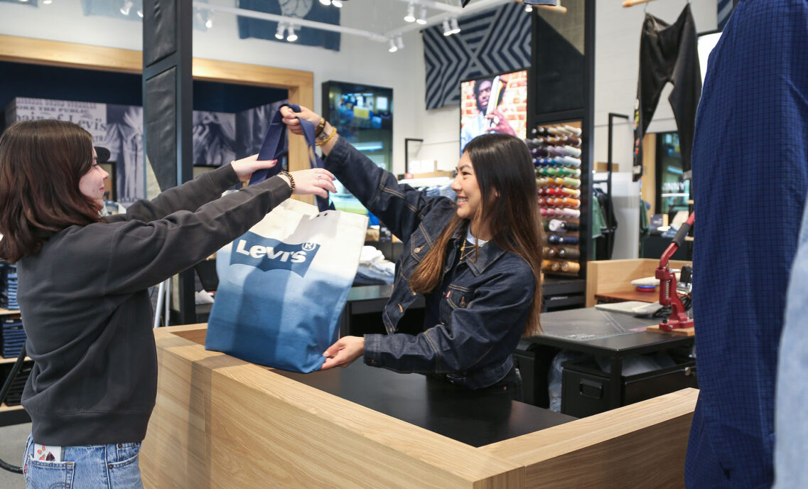 A person reaches for a Levi's® tote bag from a Levi's® retail worker as they checkout at a Levi's® store