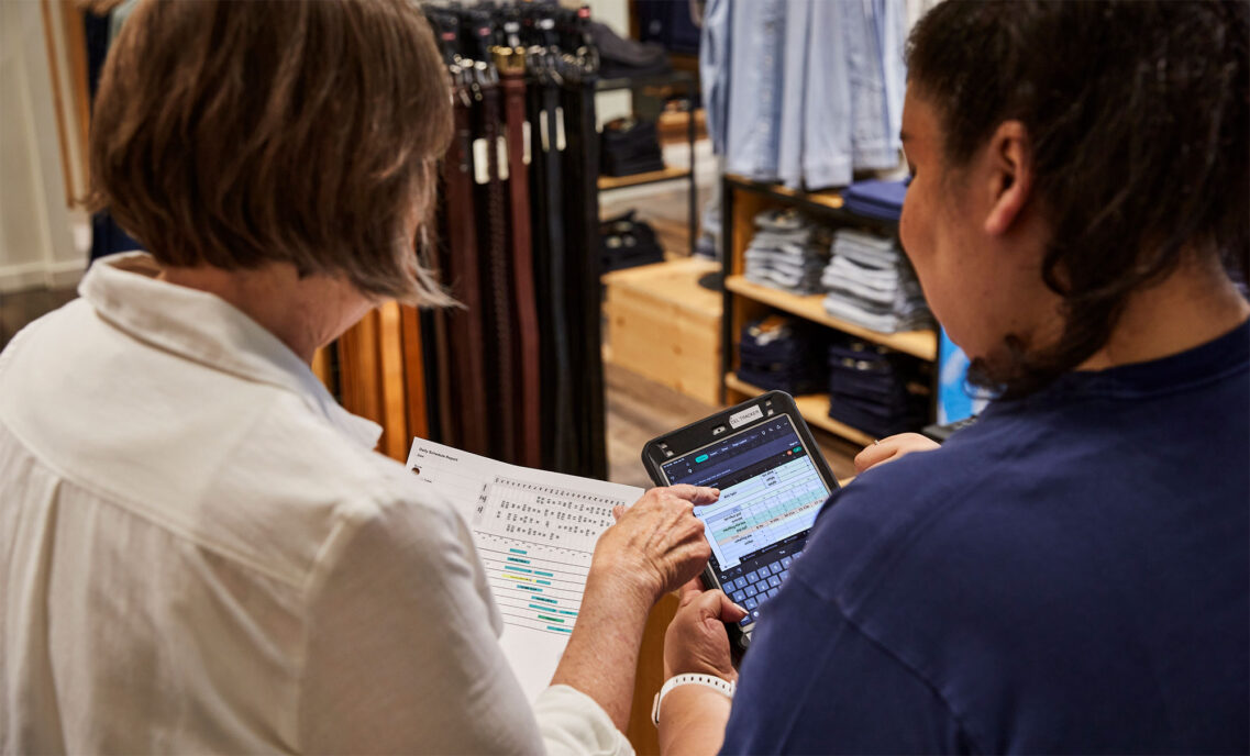 The back of two Levi's® store employees holding a scheduling sheet and referencing an electronic tablet