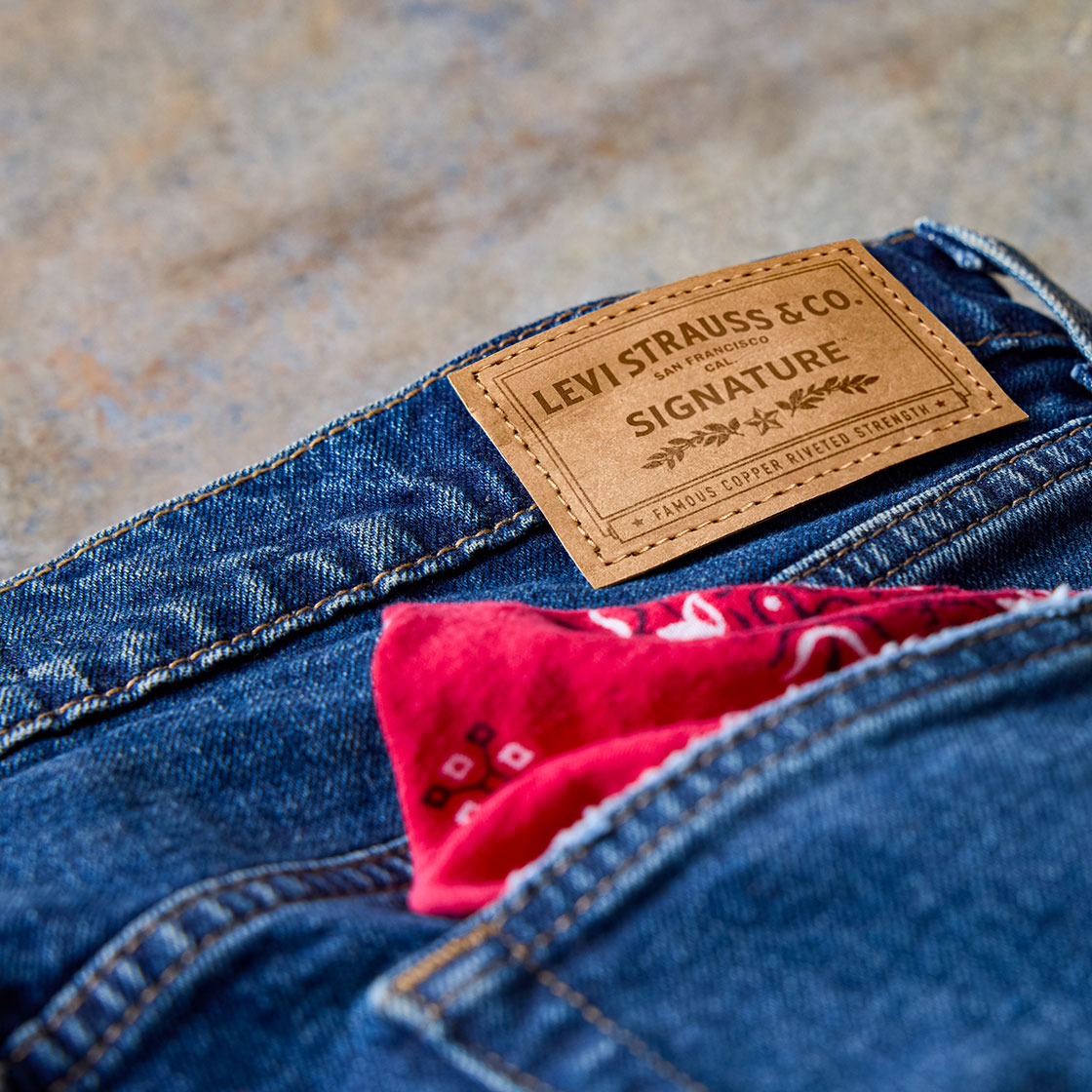 A close up of the back patch of a pair of dark wash Levi Strauss Signature denim jeans with a red bandana in the back pocket