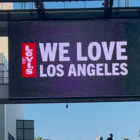 A digital sign with a Levi's® red tab logo and the text "We Love Los Angeles" hangs over a pedestrian bridge at an outdoor mall