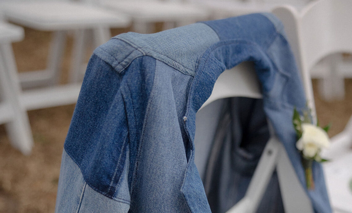 A patchwork denim jacket drapes on the back of a white chair